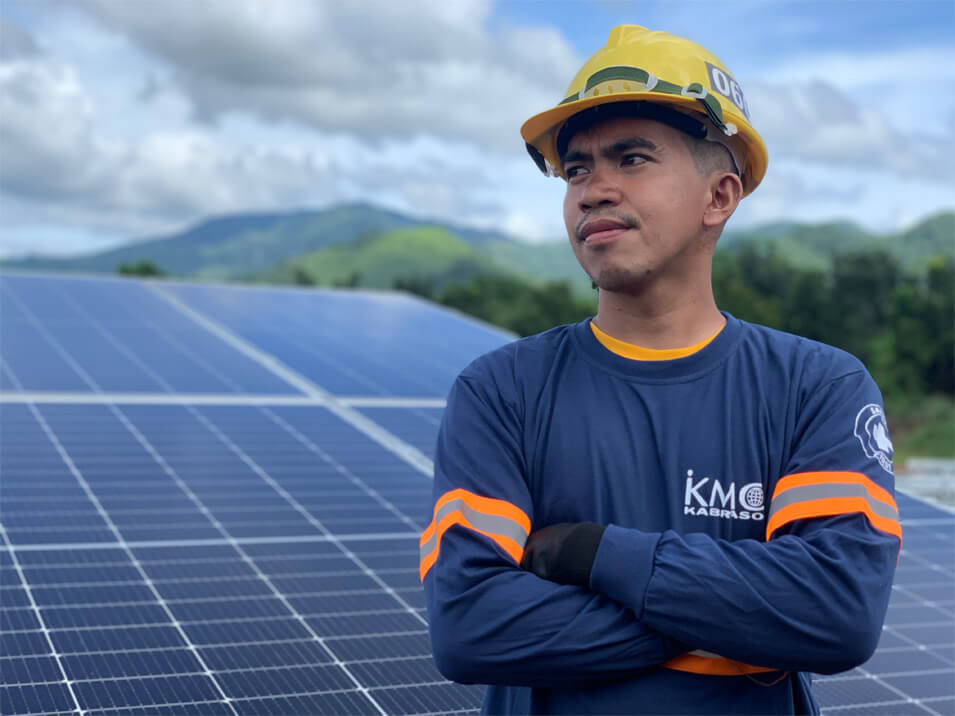KMC renewable energy employee wearing hardhat- solar panels in the bg