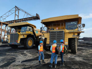 Three men in a construction area standing infront of large trucks