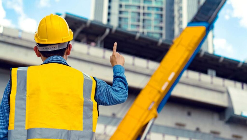 Man wearing yellow construction site safety gear pointing on a crane