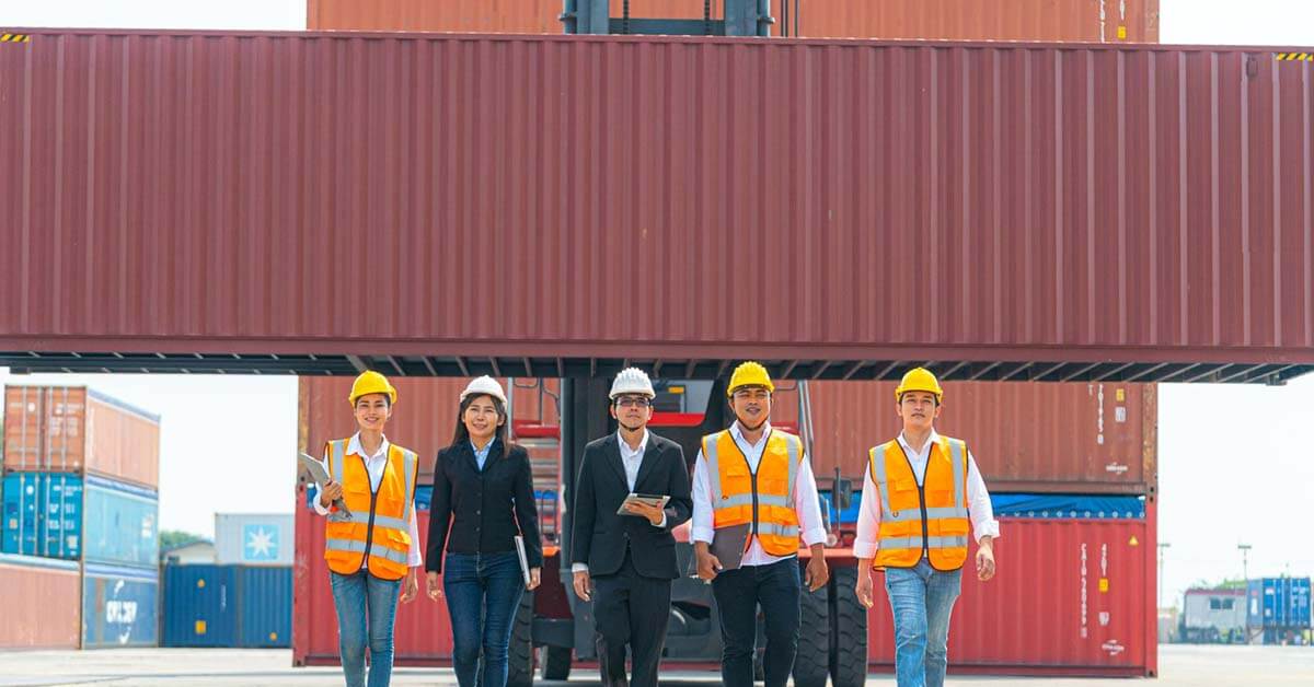 engineers and factory workers walking in front of front of machine lift container