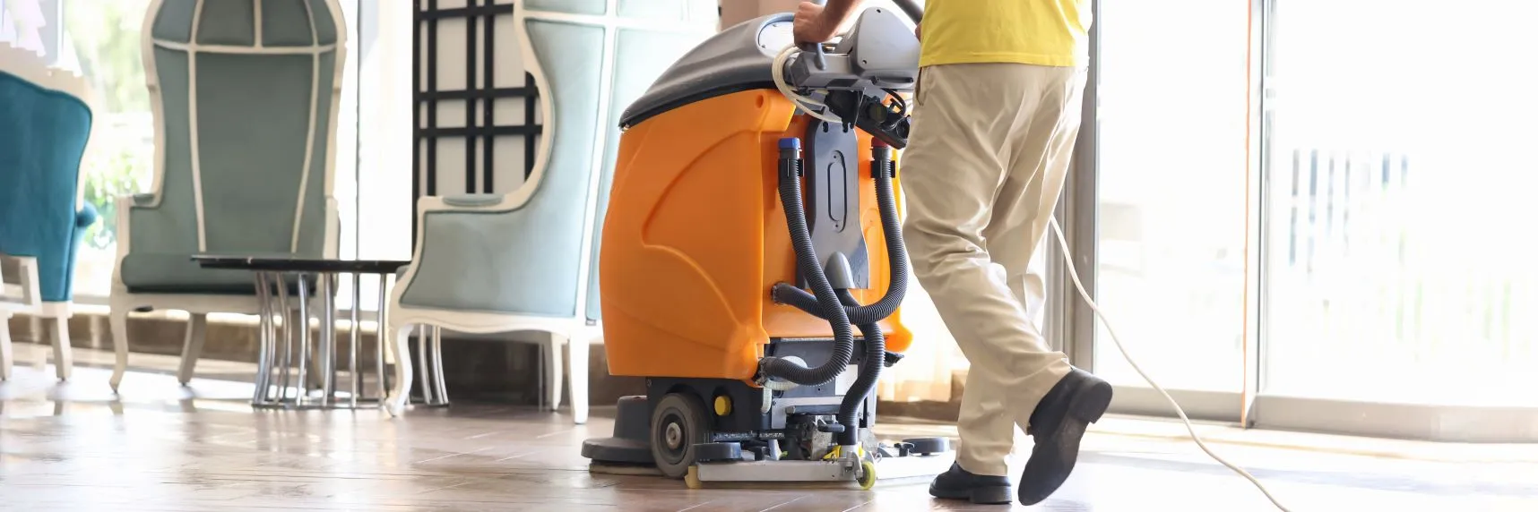 A janitor from a cleaning services company is cleaning the hall with a vacuum cleaner
