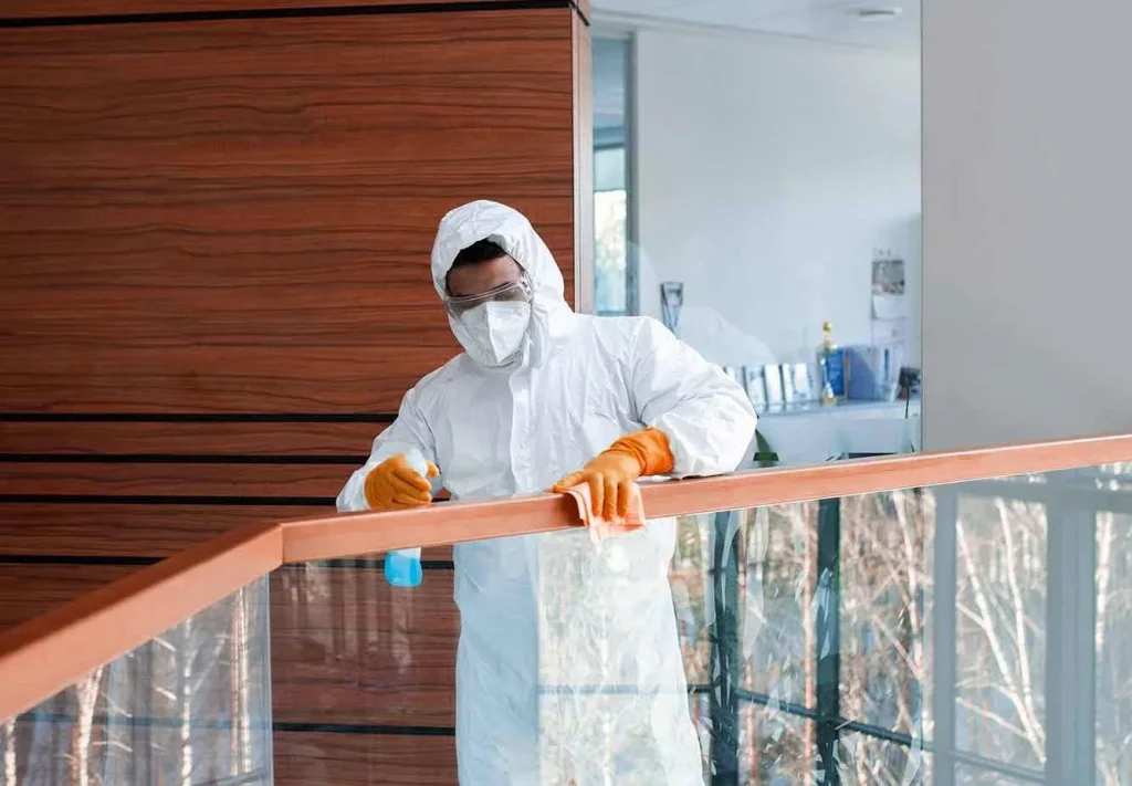 Facility management staff wearing PPE while disinfecting and sanitizing stairs handle